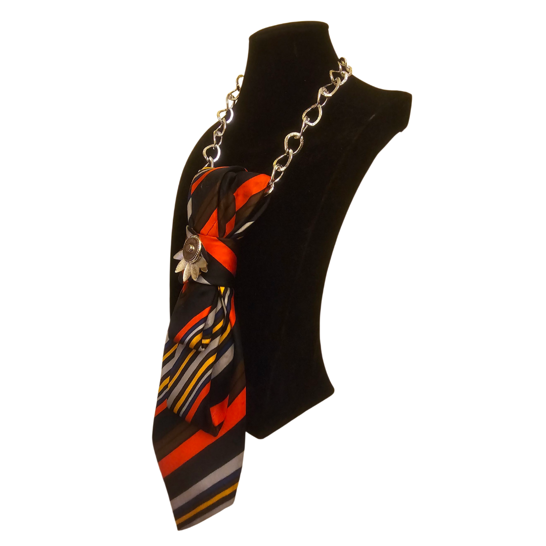 Posizione laterale su manichino Cravatta Gioiello Stripes Fire Claudia De Rosa Jewelry – collana-cravatta in tessuto vintage rigato rosso e arancio con catena silver e fermaglio magnetico floreale.